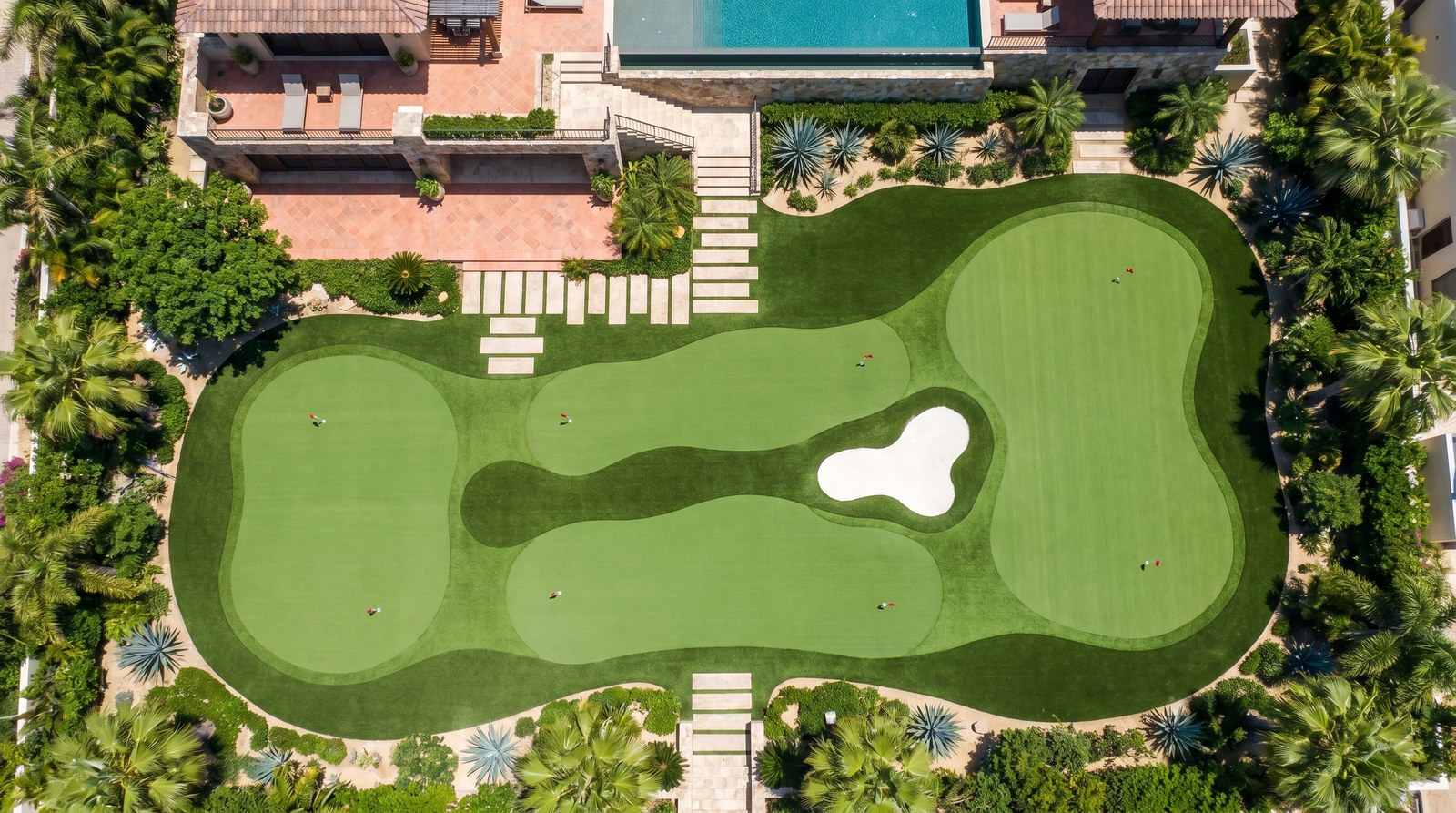 Putting green amplio con varios hoyos, breaks y chipping area en un jardín residencial